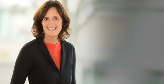 Sandra Weiß im Gespräch, lächelnd, in dunklem Blazer vor hellem Fenster