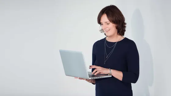 Sandra Weiß steht mit aufgeklapptem Laptop in einem hellen Raum
